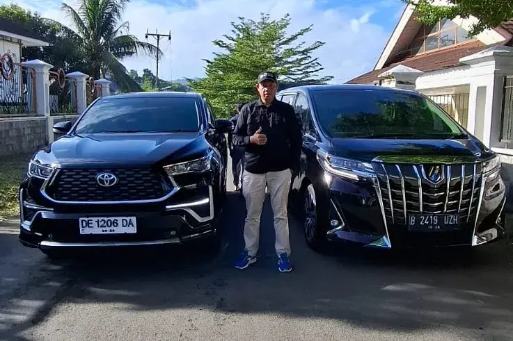 Elias Jusra, pemilik Shafira Trans, berdiri di antara dua mobil armada.